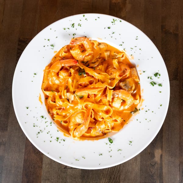 Fettuccine pasta with shrimp and mushrooms in a creamy tomato sauce, garnished with parsley.