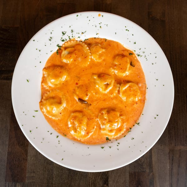 Ravioli pasta in a creamy orange sauce, garnished with parsley, on a white plate.