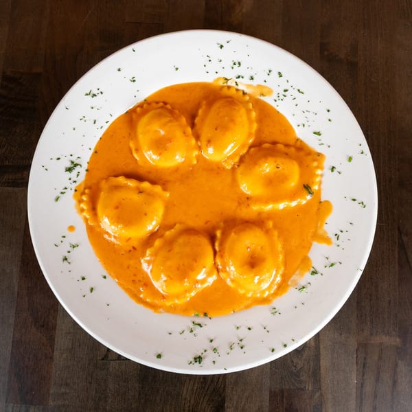 Seven ravioli pasta in a creamy orange sauce, garnished with green herbs on a white plate.