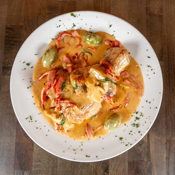 Creamy chicken dish with red peppers and green olives, garnished with parsley on a white plate.