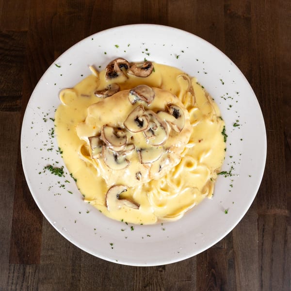 Creamy mushroom pasta dish with parsley garnish on a white plate, viewed from above.