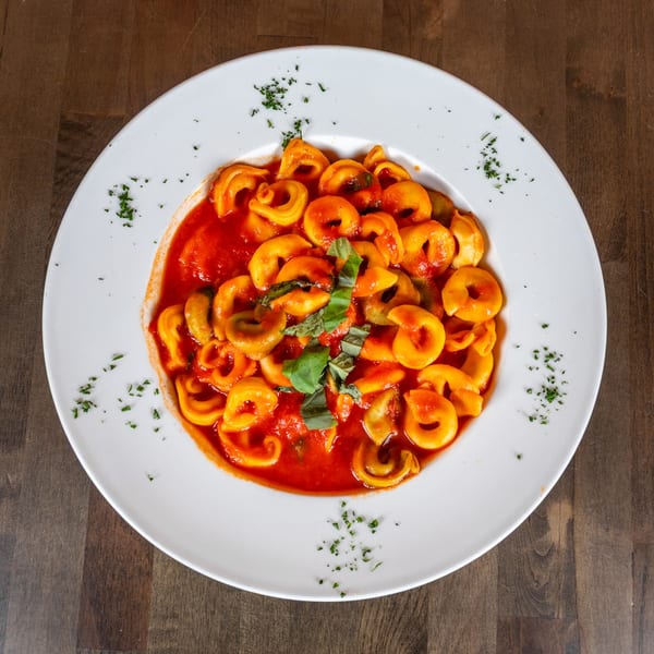Tortellini pasta in red tomato sauce, garnished with fresh basil and parsley on a white plate.